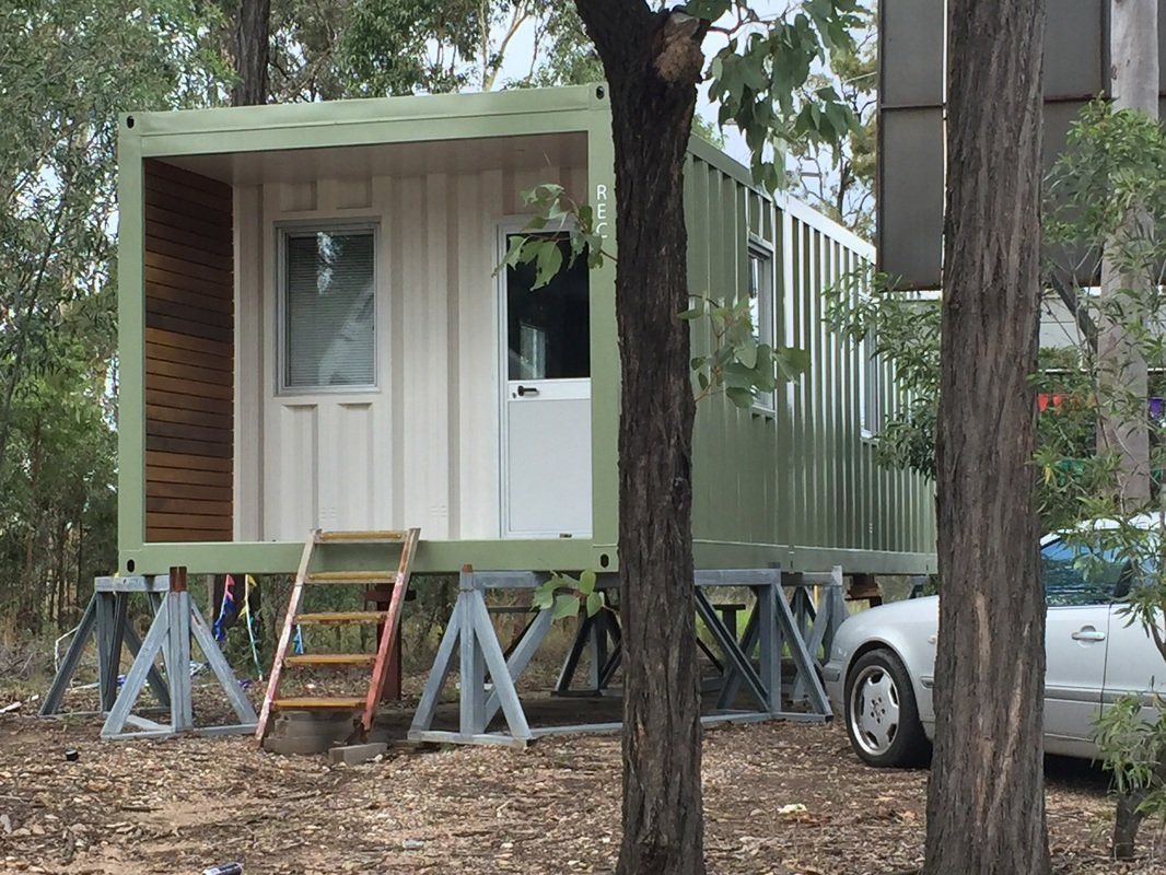 Shipping container home elevated on supports, surrounded by trees.