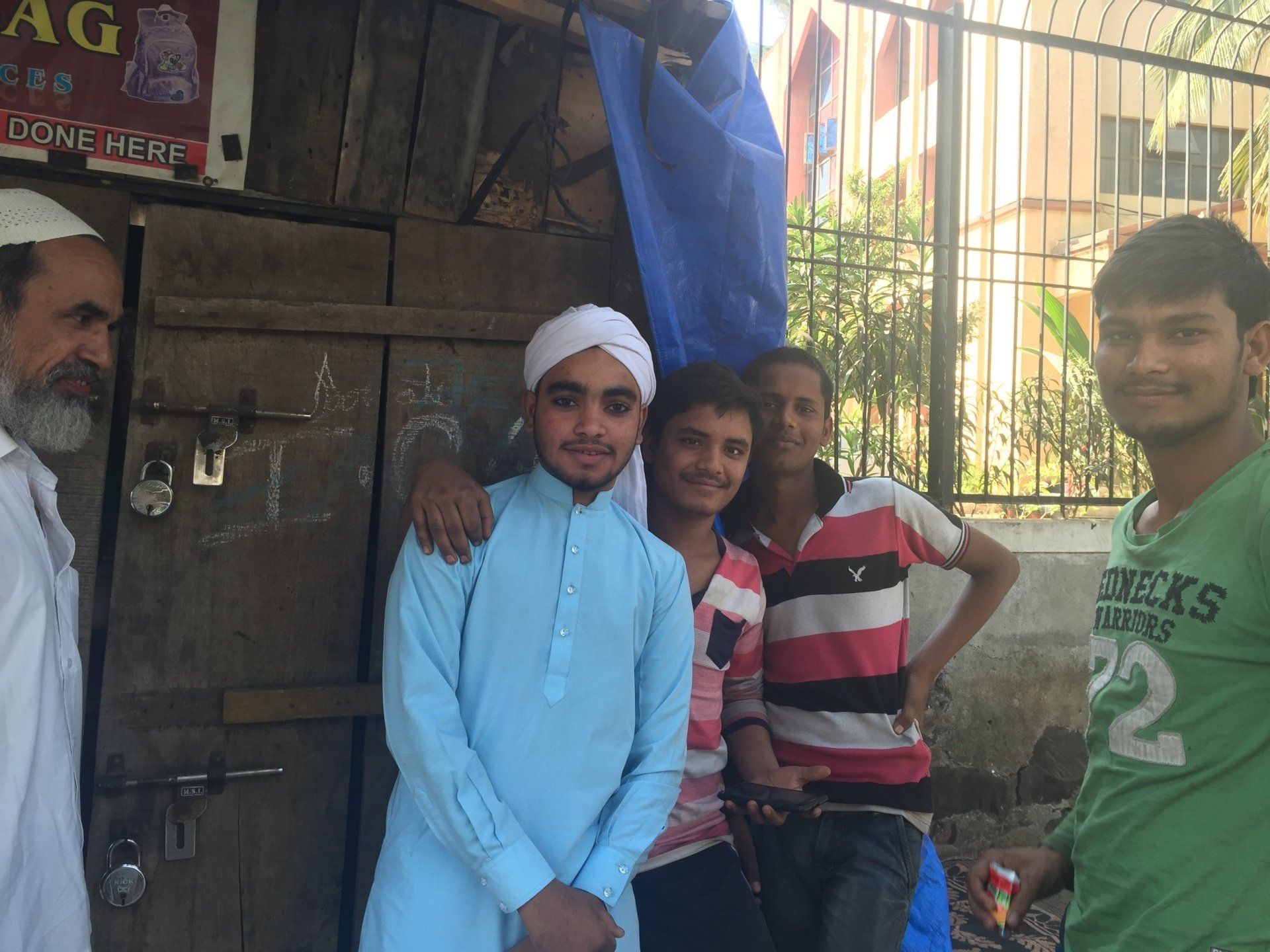 Group of people posing by a wooden door. One man in a turban and light blue shirt smiles. Others smile.