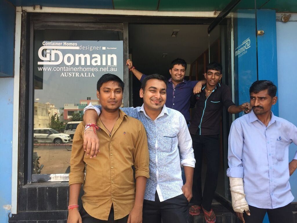 Five people pose outside a business with glass doors. One has a wrapped arm. The logo reads