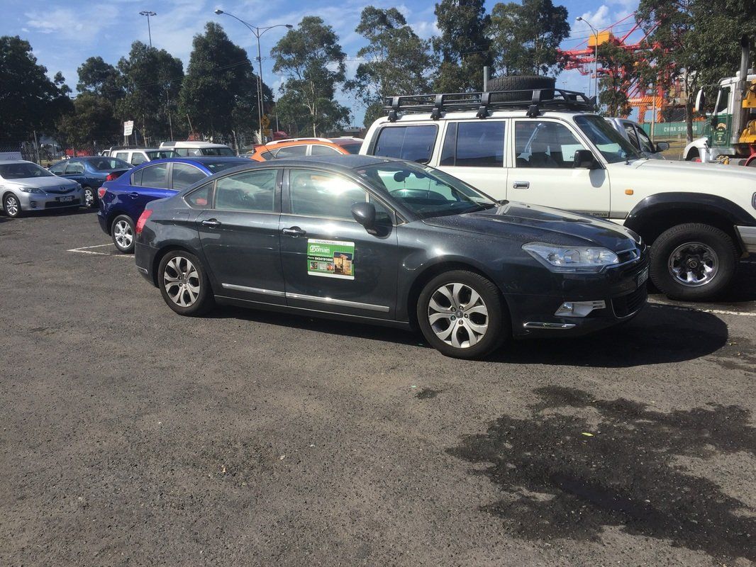Dark gray car parked in a lot, with other vehicles in the background. Sunny day.