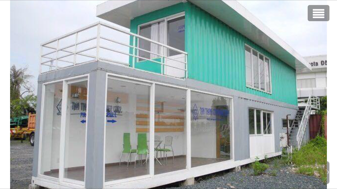 Two-story building with teal upper level, glass-walled ground level. Balcony and exterior stairs.