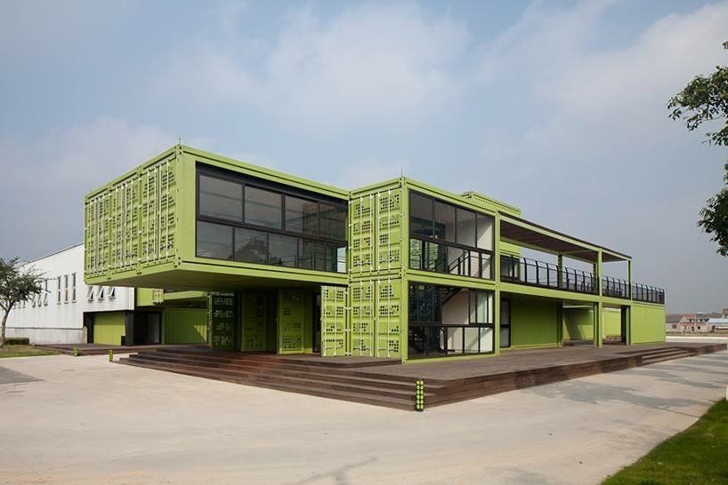 Green shipping container building with large windows and a covered patio.