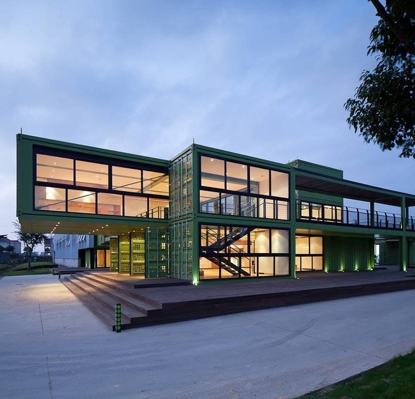Green shipping container building with large windows and wooden deck.