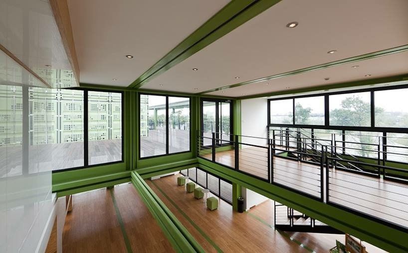 Two-story interior with large windows, green trim, and a wooden floor. A railing surrounds the upper level, overlooking the lower.