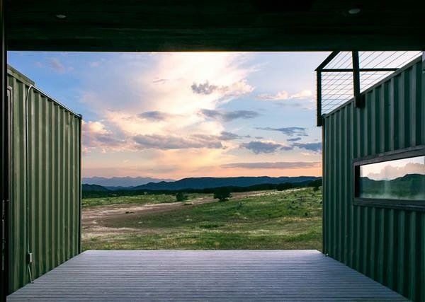 Open green shipping container with a view of a grassy field, mountains, and sunset sky.