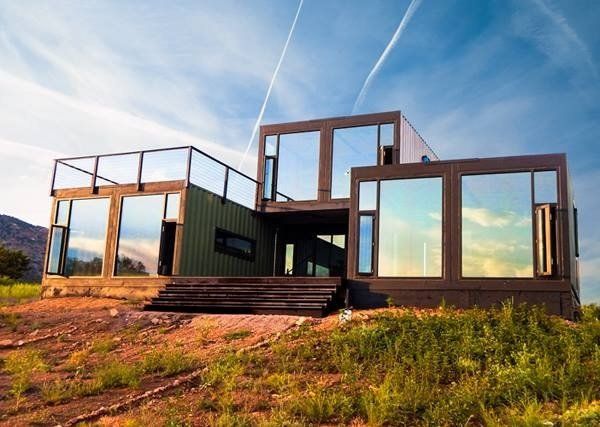 Modern house made from shipping containers, with large windows, set on a hillside.