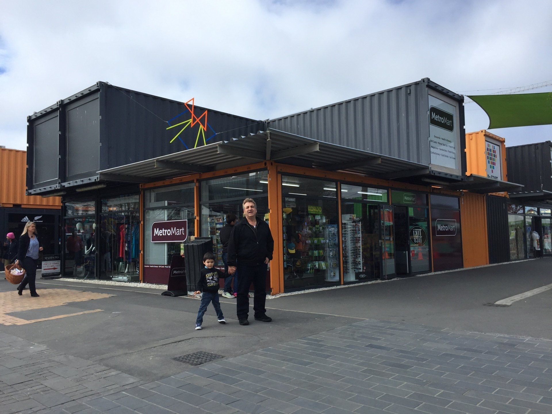 Shops made from shipping containers with people walking nearby on a cloudy day.