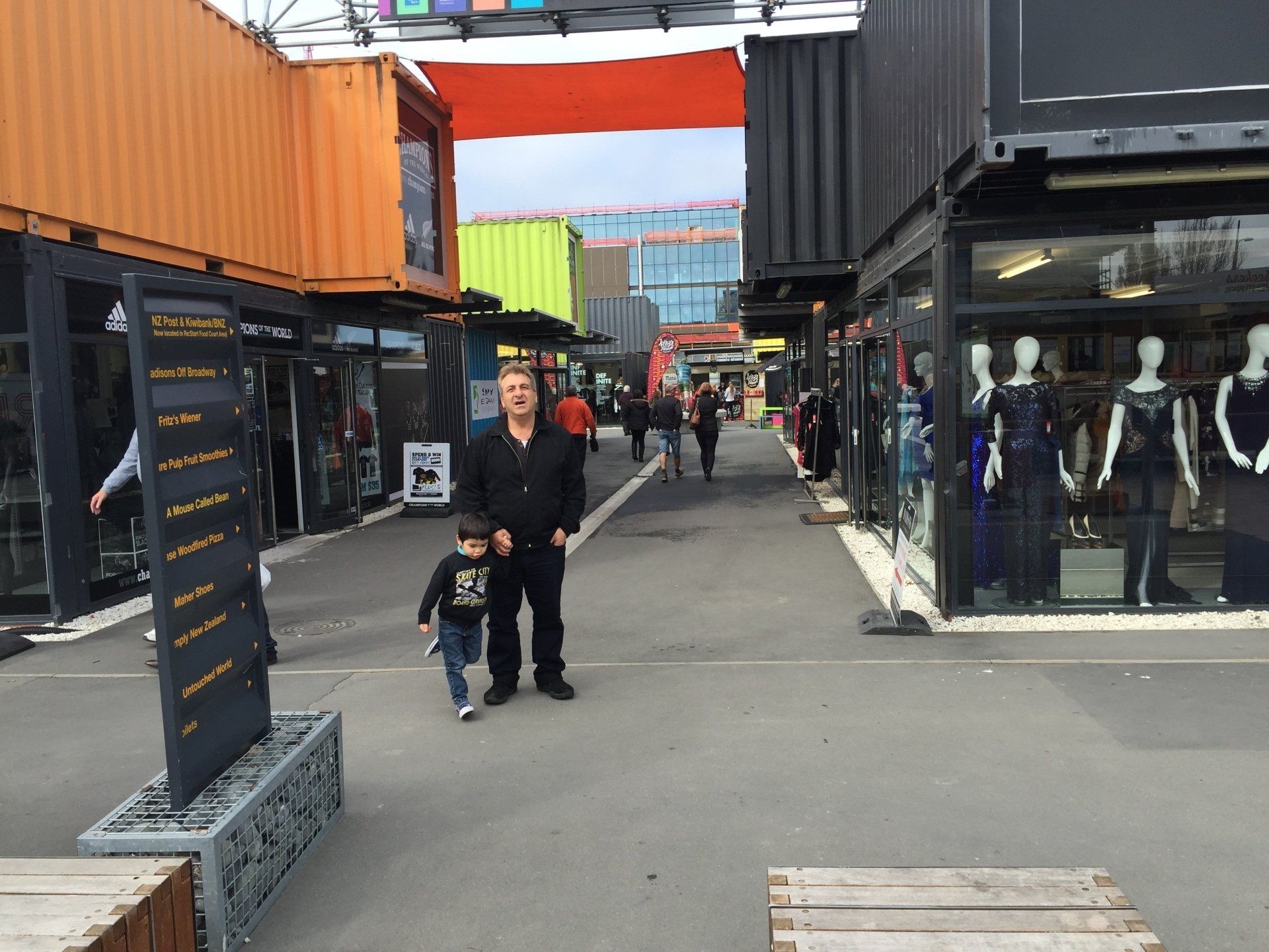 Man and child walking through a marketplace of colorful shipping containers with shops.