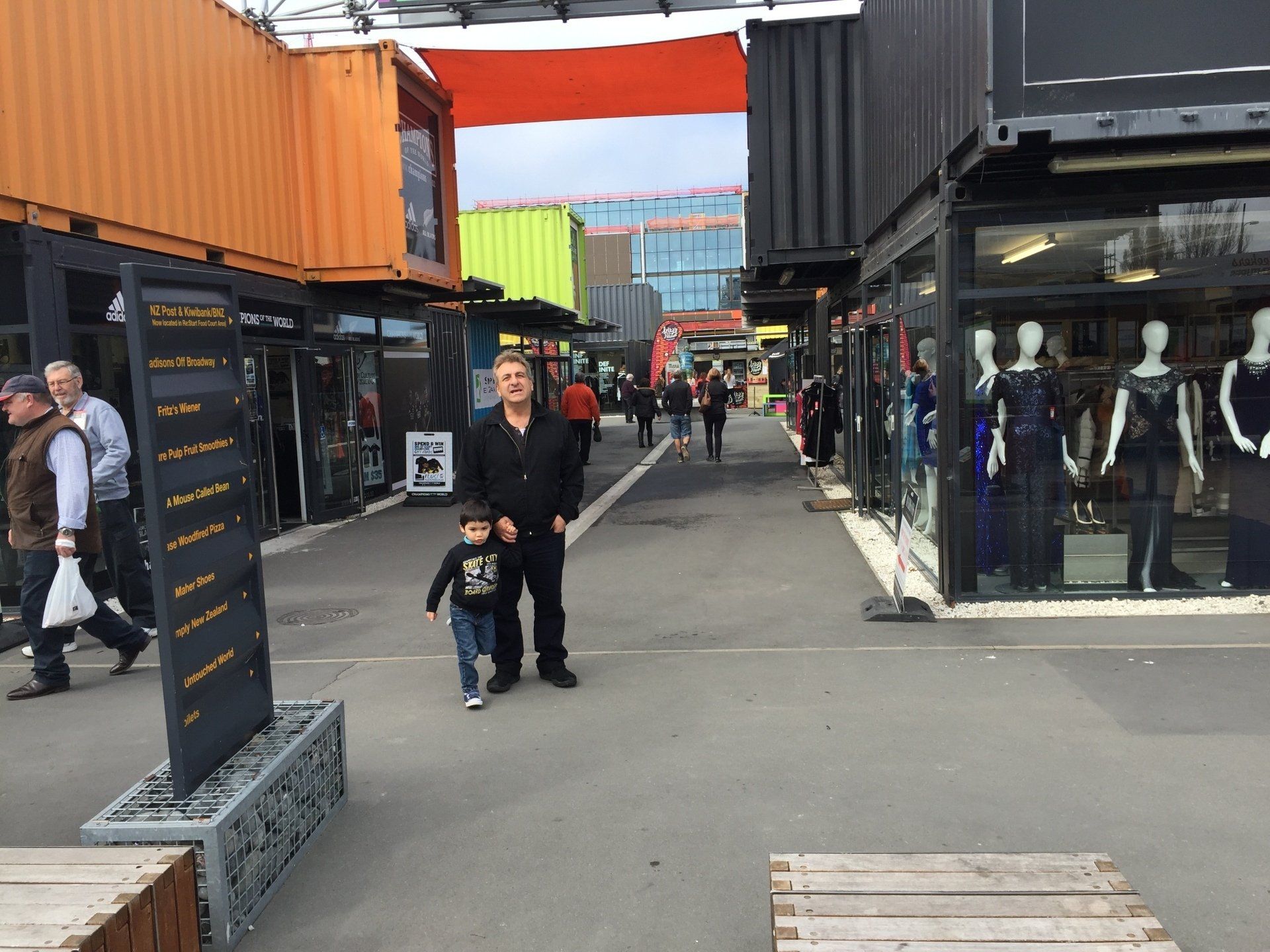 Man and child walk down a shopping street lined with shops built from shipping containers.