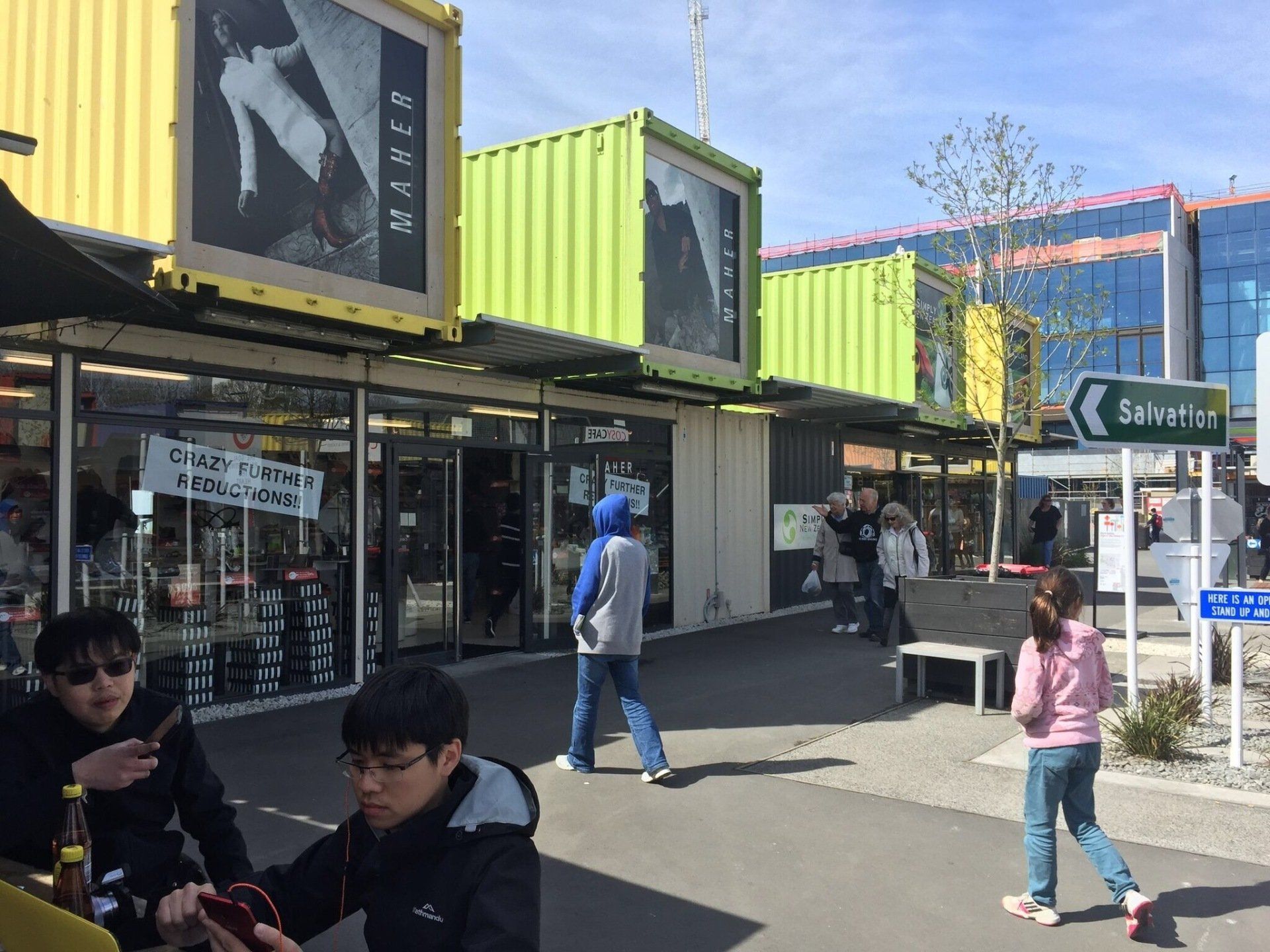 Shops in brightly colored shipping containers; people walk and sit outside on a sunny day.