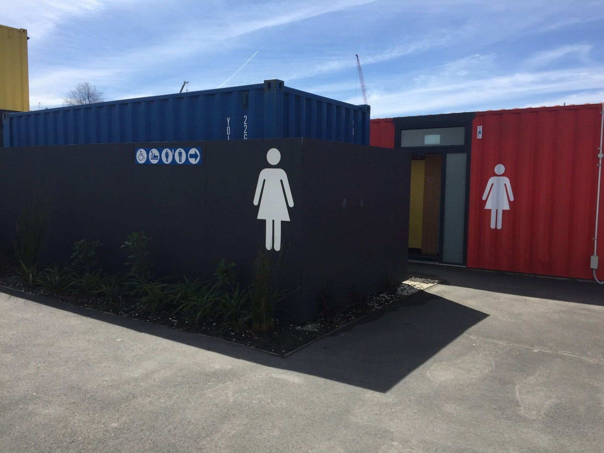 Public restrooms in converted shipping containers, with women's symbols. Blue, red, and yellow containers.