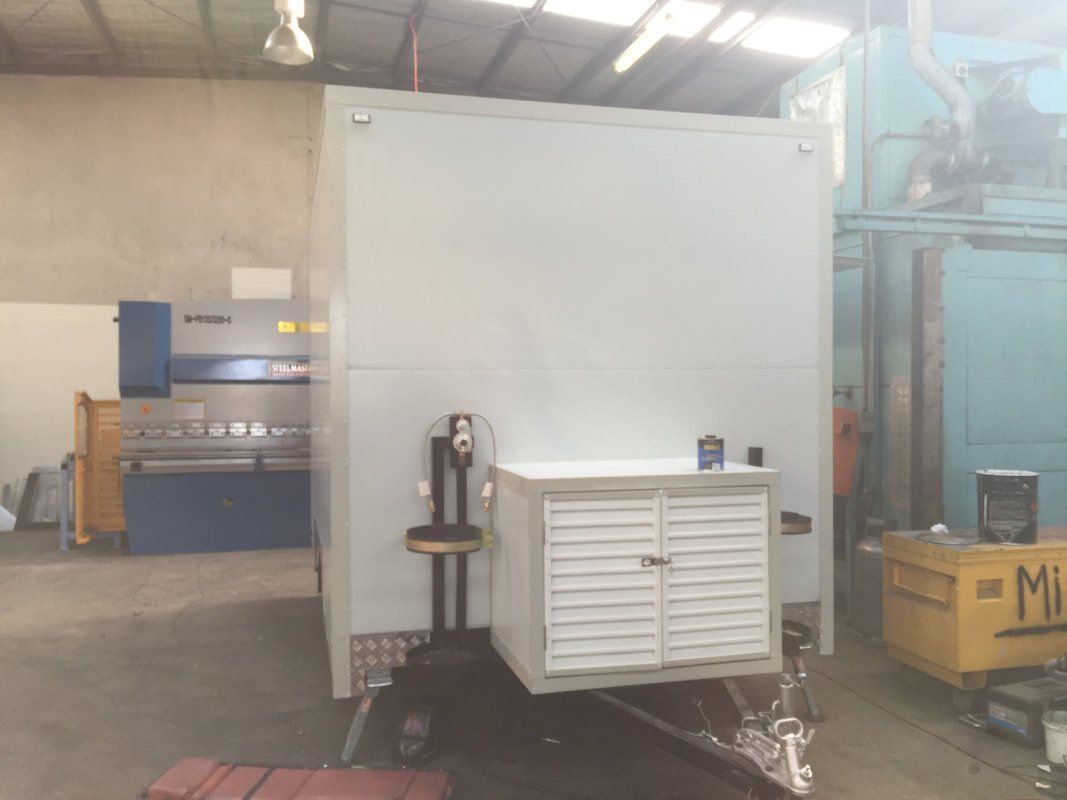 White trailer with storage cabinet attached, in a workshop setting with machinery.