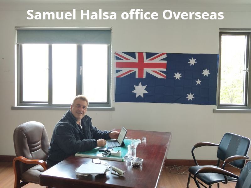 Man seated at a desk in an office with an Australian flag; windows visible.