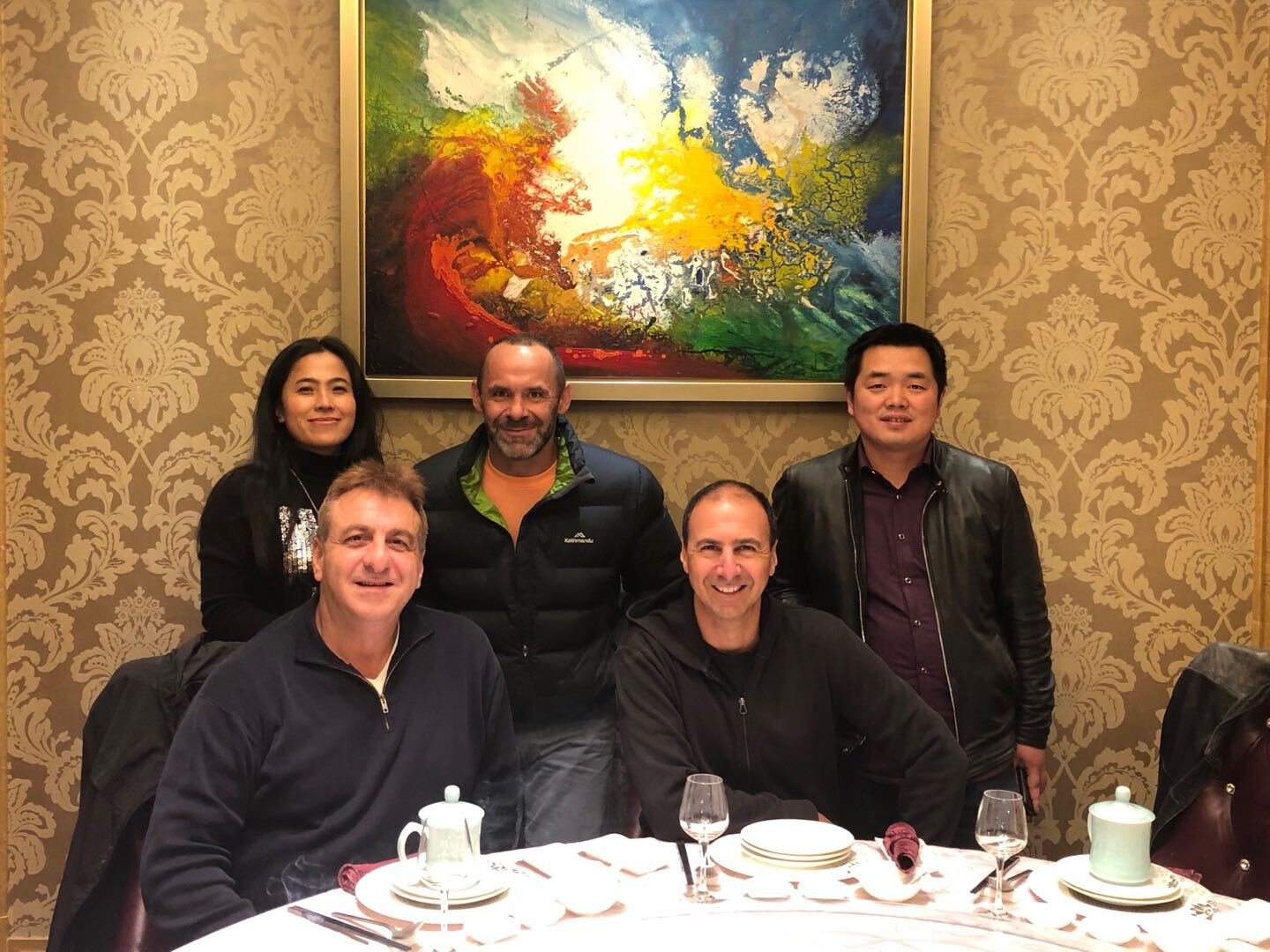 Group of five people at a restaurant, seated around a table with a painting in the background.