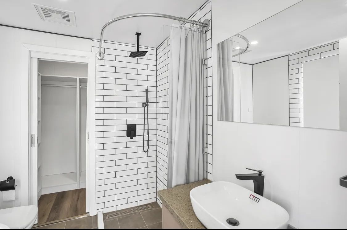 Modern bathroom with white and black tile shower, oval sink, large mirror, and open doorway to a closet.