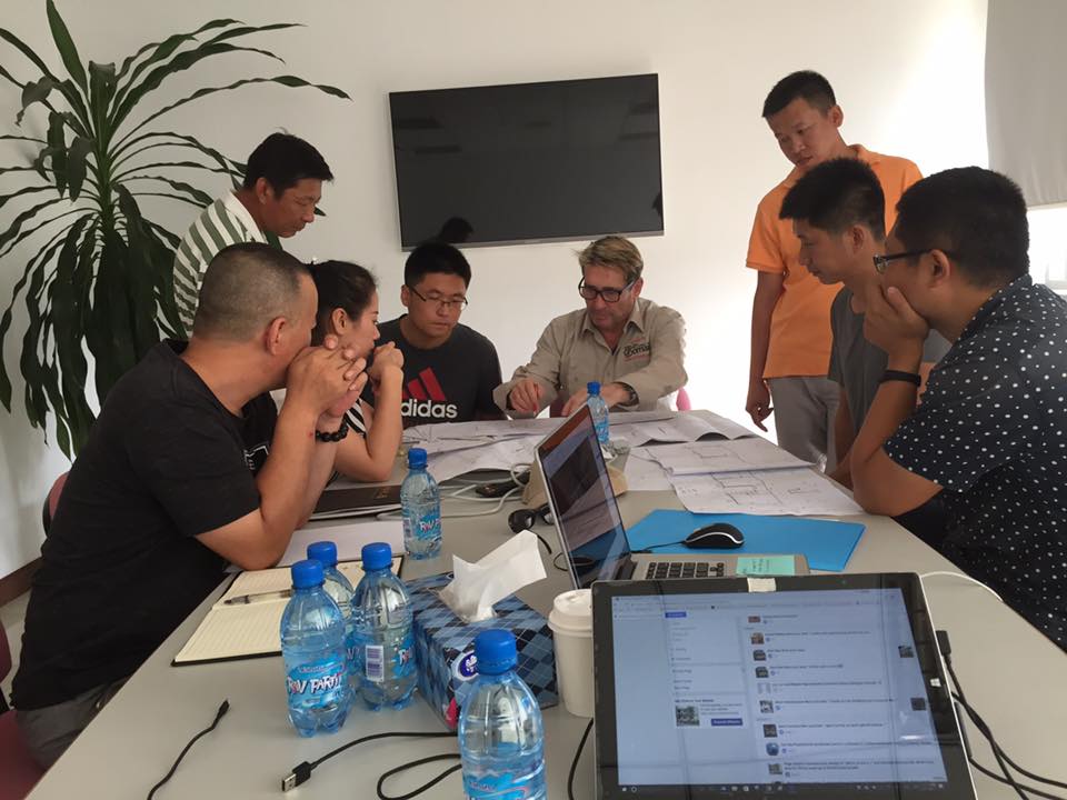 People gathered around a table with laptops, documents, and water bottles, discussing and collaborating in an office setting.