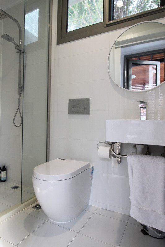 Modern white bathroom with a toilet, sink, shower, and mirror.