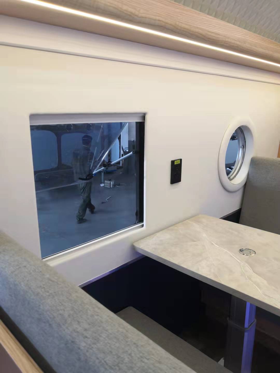 Interior of a train car with a table, seats, window, and wall features. A person is visible outside.
