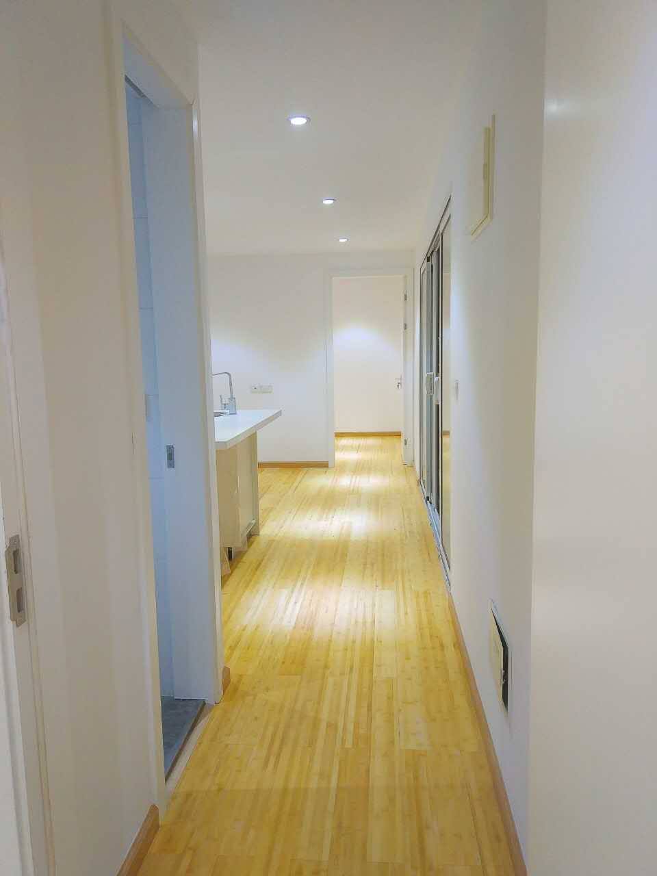 Hallway with wooden floor, white walls, recessed lighting, and doors leading to other rooms.