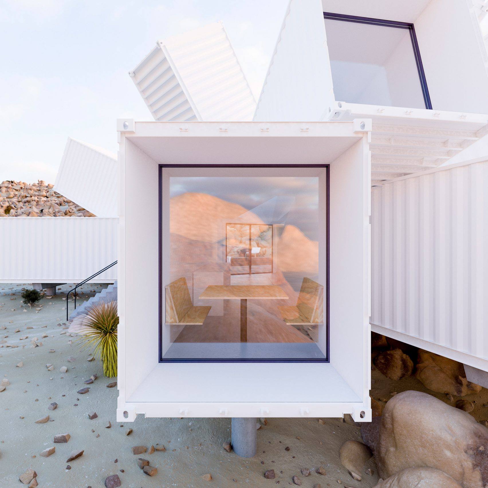 White shipping container home with large window, chairs, and table. Desert backdrop.