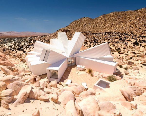 White angular home built from shipping containers in a desert landscape with rocky terrain.