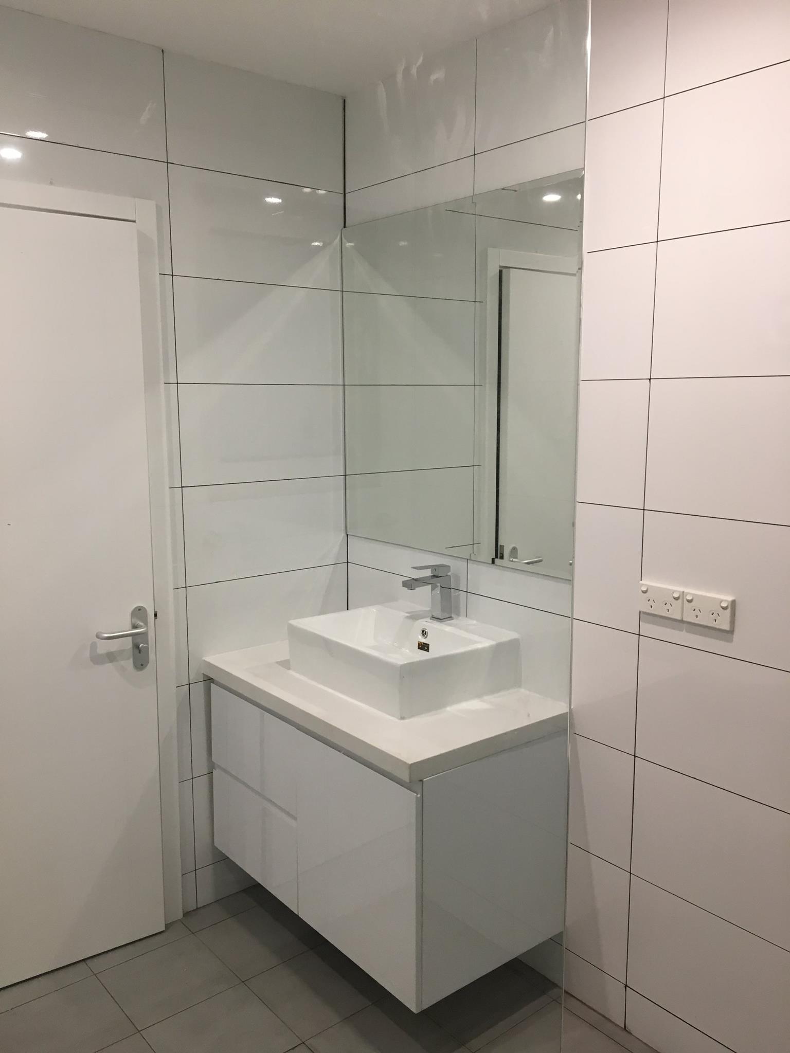 White modern bathroom with floating vanity, sink, mirror, and door.