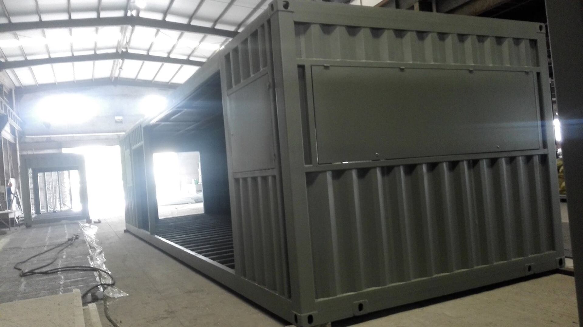A modified green shipping container with a large opening, inside a workshop.