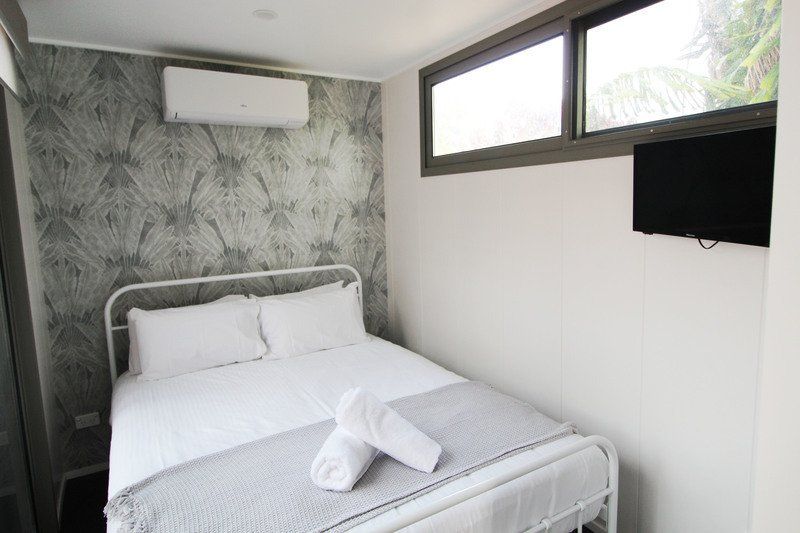 Bedroom with white bed, gray bedding, small TV, window, air conditioner. Gray patterned wallpaper.
