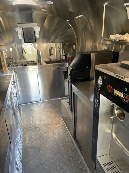 Interior of a stainless steel food truck with counters, appliances, and equipment.