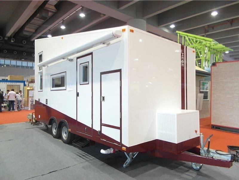 White and maroon tiny home trailer with an awning on display at a trade show.