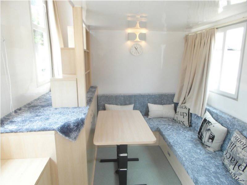 Small interior, with built-in seating, a table, window, and clock on the wall.