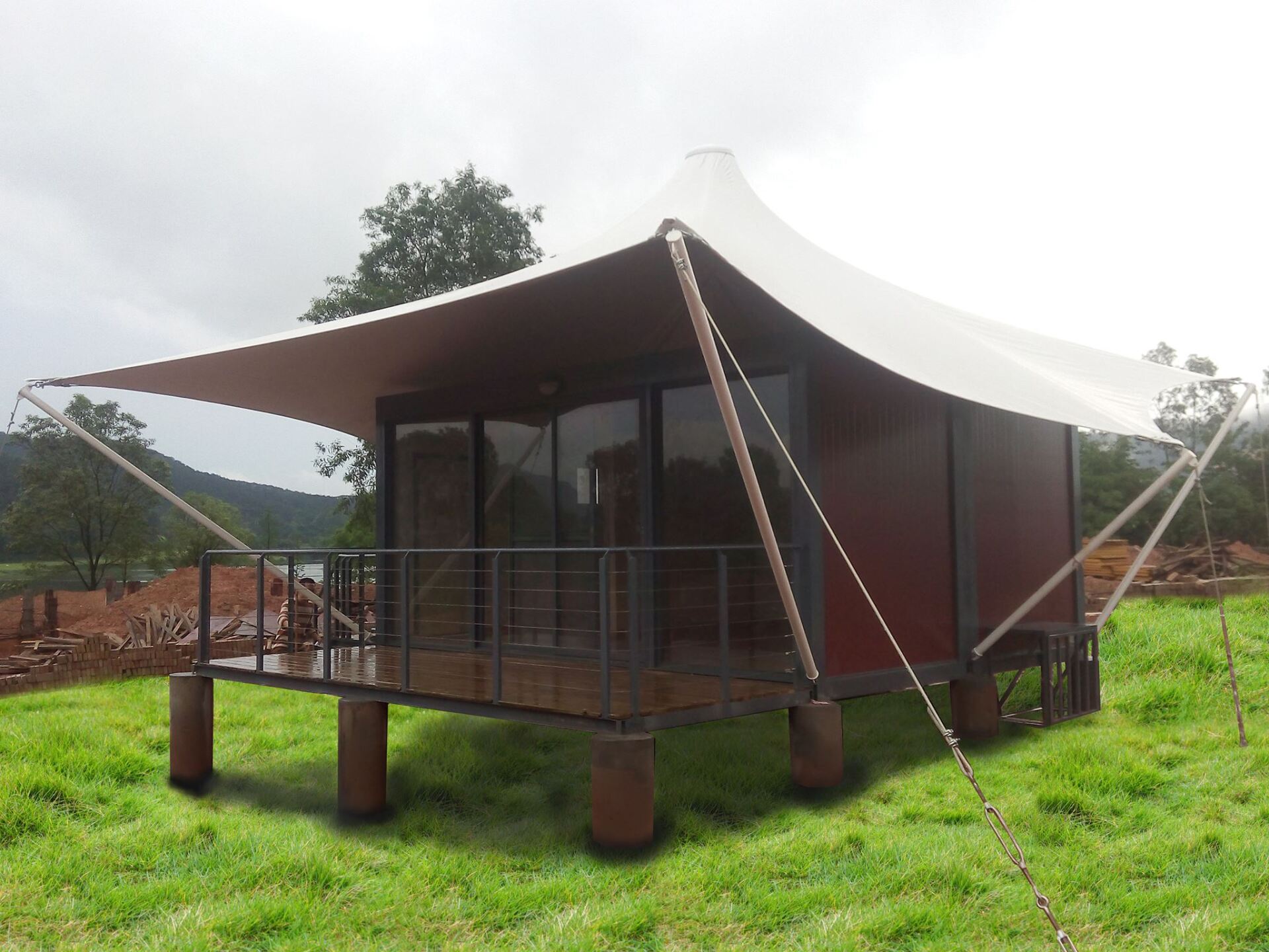 Tent-like structure with a deck, dark brown walls, and a white canopy in a grassy field.