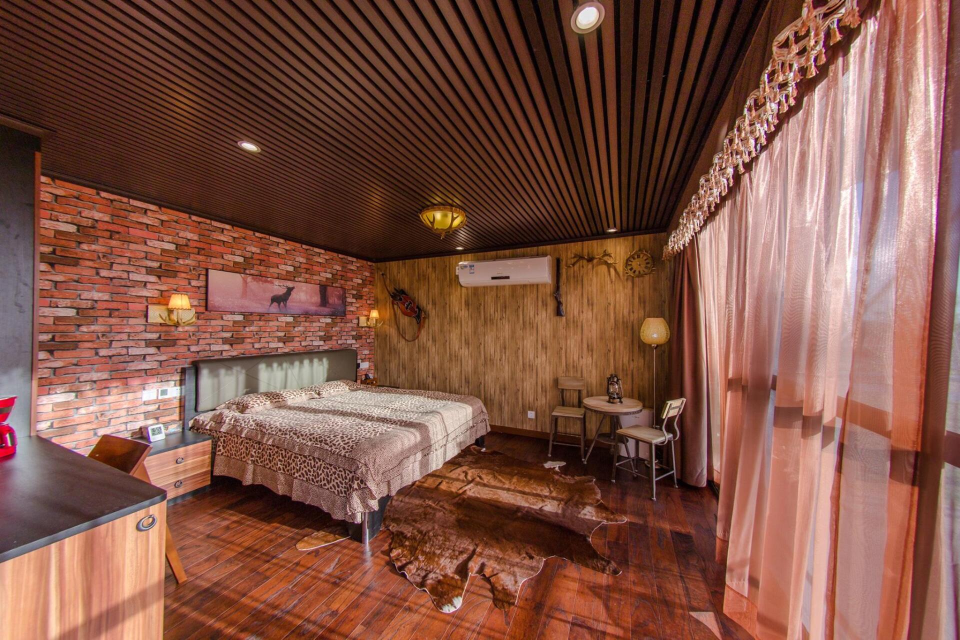 Bedroom with brick and wood walls, bed, small table and chairs, and long curtains.