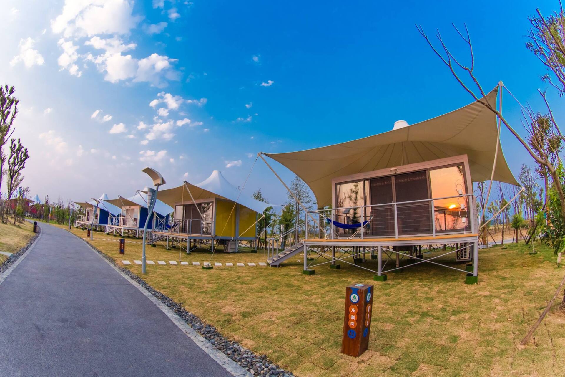 Glamping tents with canvas roofs line a walkway on a sunny day.