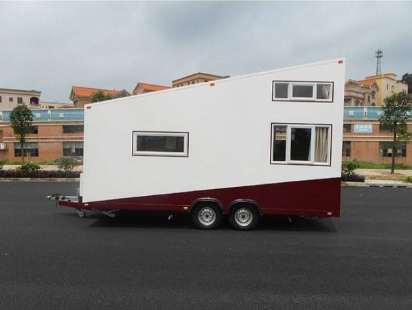 White and maroon tiny house on wheels, with angled roof and two windows, parked outdoors.