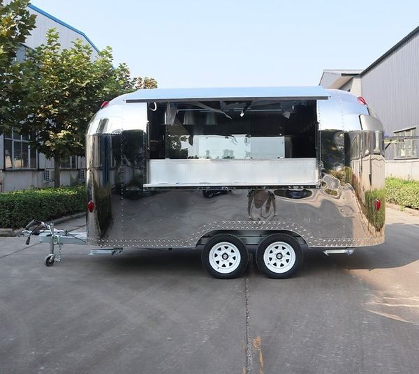 Shiny silver food trailer with open serving window, white wheels, parked outdoors.