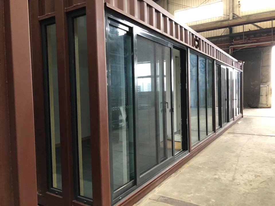 Brown shipping container with large sliding glass doors, likely a repurposed structure indoors.