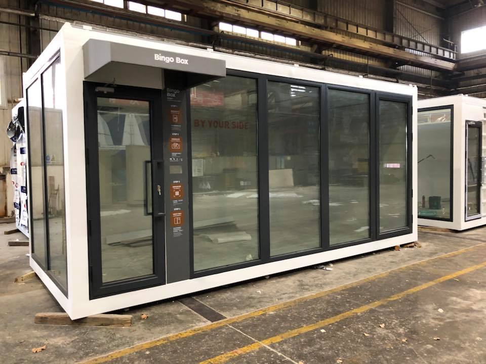 Modular building with large glass windows and black trim, likely a commercial space, in an industrial setting.