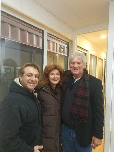 Three people standing close together; one in a hooded jacket, one in a coat, and one with a scarf and a blazer.