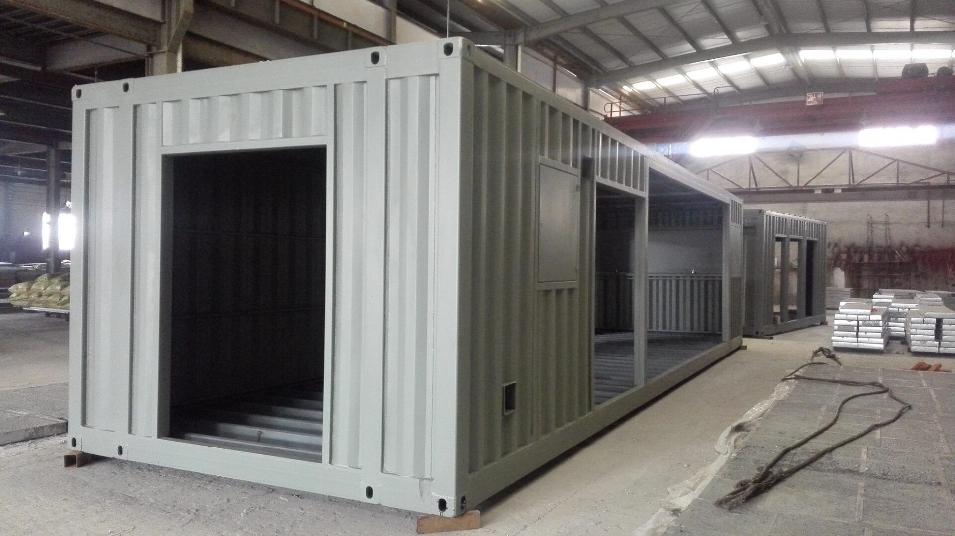 Metal shipping containers modified with openings for doors and windows in a workshop.