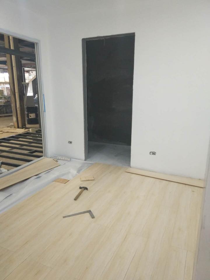 Interior room under construction: light wood flooring, doorway, white walls, and exposed framing.