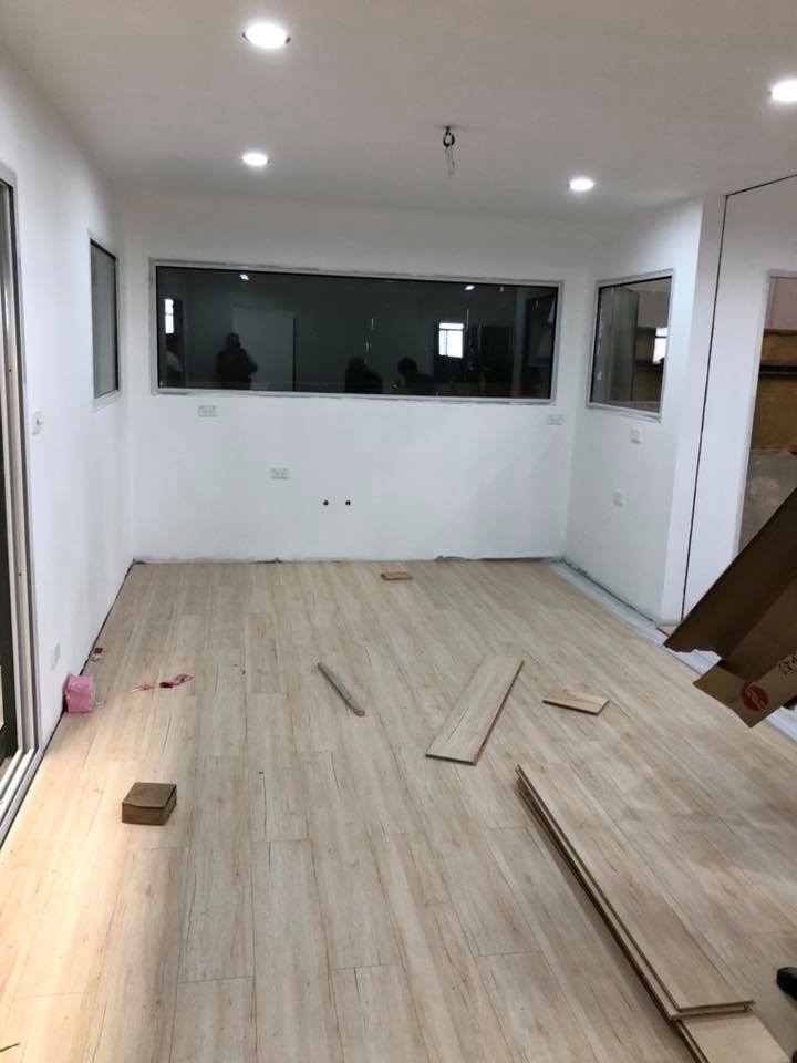Room under construction with new flooring. Light wood planks, white walls, large window.