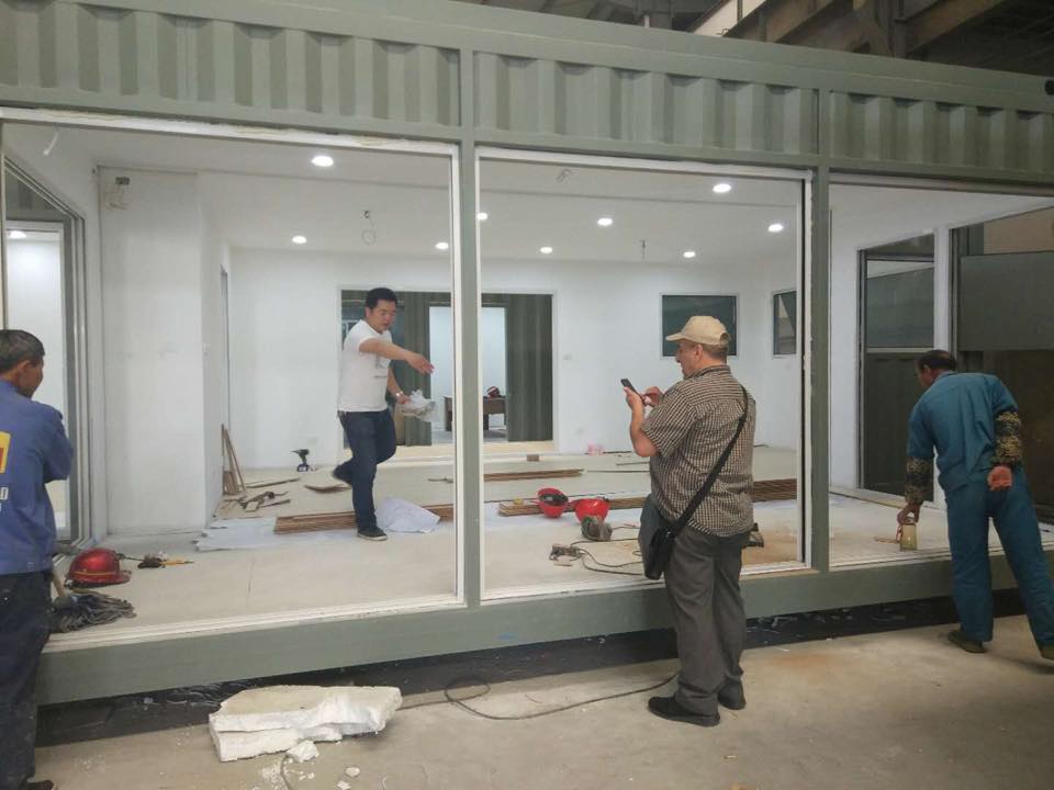 Workers installing windows in a modular building. People stand inside and outside, some taking photos.