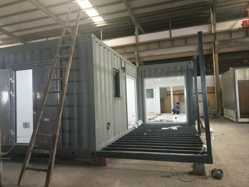 Metal shipping containers being modified for a building; a person works inside.