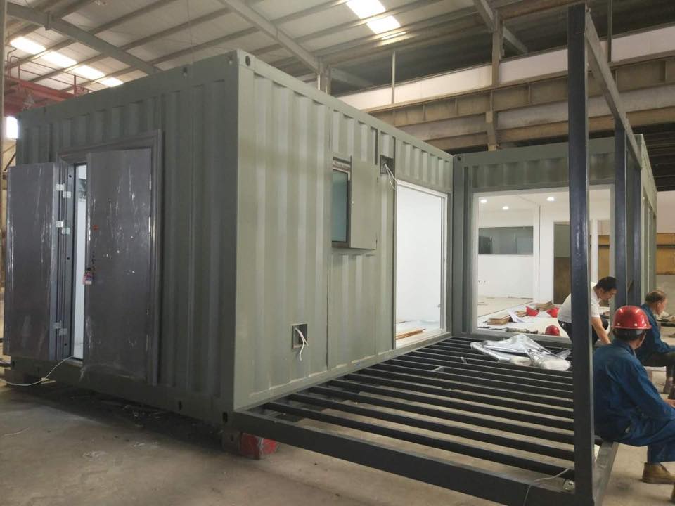 Two shipping containers joined, modified into a structure with open doors and a ramp. Workers are visible.