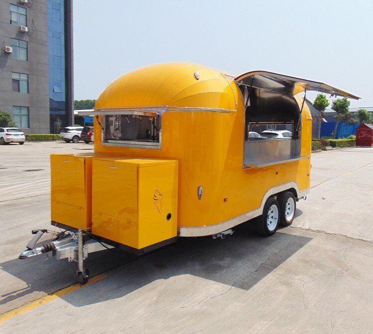 Yellow food trailer with open serving window, parked outdoors.