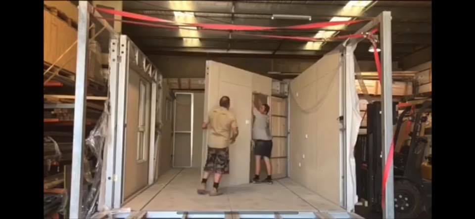 Two people installing a large wall panel inside a metal structure, likely a building under construction.