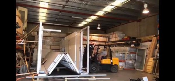 Forklift operator in a warehouse moves building materials, including panels and frames.