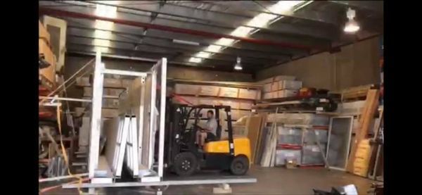 A forklift in a warehouse is transporting framed windows and doors on a pallet.