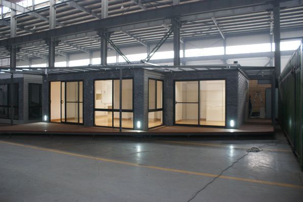 Modern modular building inside a large industrial structure, featuring large windows and an outdoor deck.